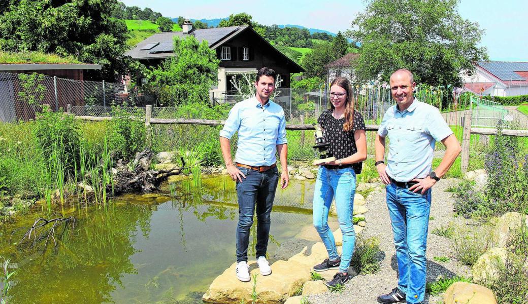 Prorektor Marc Caduff (v. l.) und Malin Wiget überreichen Schulleiter Roland Bösch vor dem Biotop eines von fünf Mikroskopen. 