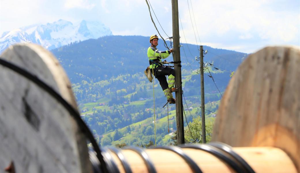 In luftiger Höhe wird das Freileitungsrohr für die Glasfasern an die bestehenden Masten angebracht. 