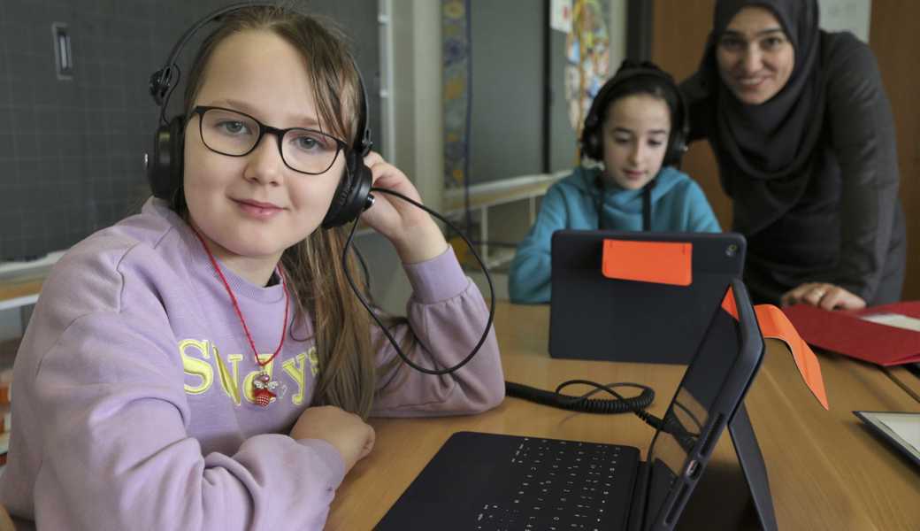 Auf Schulbesuch in der Integrationsklasse: Diana aus der Ukraine arbeitet am Laptop, eine Klassenassistentin hilft bei Fragen. 