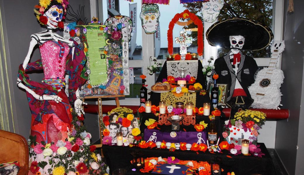 Mit einem reich geschmückten Altar werden die Verstorbenen an die Familientafeln gerufen. Links die Calavera Catrina.