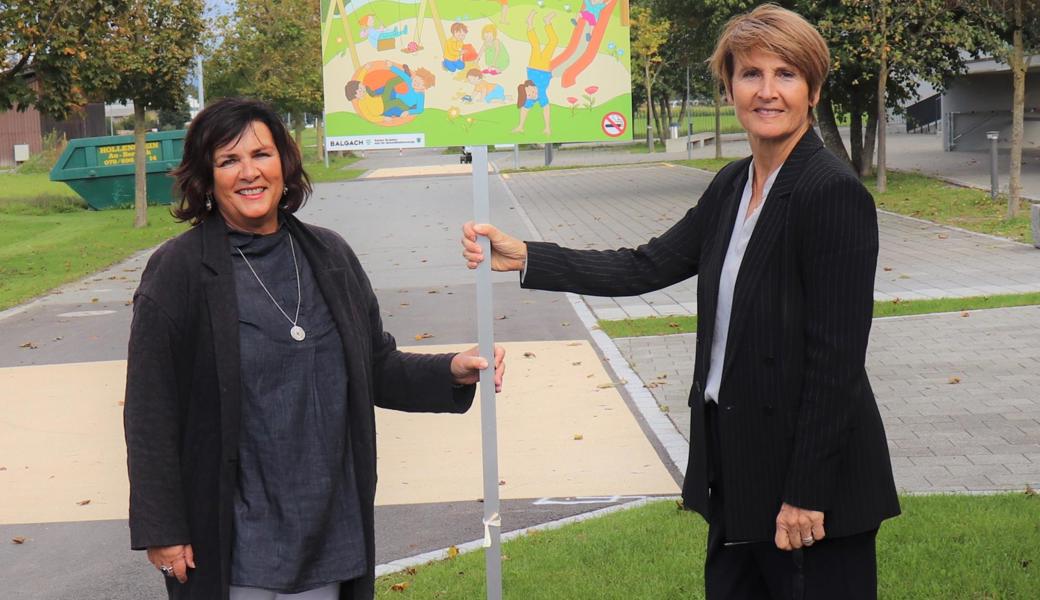 Jolanda Welter Alker und Silvia Troxler beim Schild, das darauf hinweist, dass der Kinderspielplatz eine rauchfreie Zone ist.