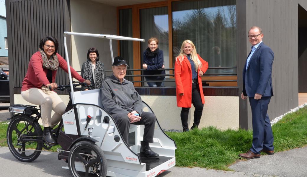  «Augiessen»-Bewohner Hans Bösch sitzt zum ersten Mal in der e-Rikscha, gesteuert von Conny Haas. Hinten von links: Angela Bösch, Yvette Werner, Antonia Schegg (Leiterin Marketing) und Thomas Haas, (Vorsitzender Bankleitung) von der Raiffeisenbank Mittelrheintal.